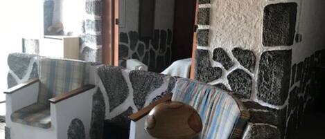 Une pièce aux murs de pierre, dotée d’un plafond en bois, d’une cheminée en pierre et d’un fauteuil à rayures.
