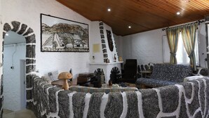 A cozy living room with a stone fireplace, a wooden ceiling, and a colorful sofa. - Refúgio Saloio in Lousa-LRS (Lousa)