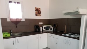 Eine Küche mit weißen Schränken, einem Gasherd, einer Mikrowelle, einem Spülbecken und einem Fenster mit Vorhängen.