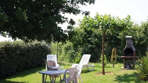 Eine Terrasse mit Tisch und Stühlen, einem Grill und einem Baum, der Schatten spendet.