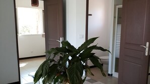 Ein Essbereich mit einem Tisch, bedeckt mit einer gemusterten Tischdecke, umgeben von weißen Stühlen. In der Mitte des Tisches steht eine Topfpflanze.