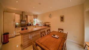 A modern kitchen with wooden countertops, a central island, and a dining area with a wooden table and chairs. - MacKenzie Cottage - Family Friendly Cottage on the Beautiful Blairquhan Estate (Maybole)