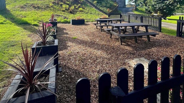 A castle-like building with a grassy hill, picnic tables, and a wooden fence. - MacKenzie Cottage - Family Friendly Cottage on the Beautiful Blairquhan Estate (Maybole)
