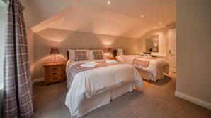 A bedroom with two beds, a nightstand with a lamp, and a mirror on the wall. - MacKenzie Cottage - Family Friendly Cottage on the Beautiful Blairquhan Estate (Maybole)