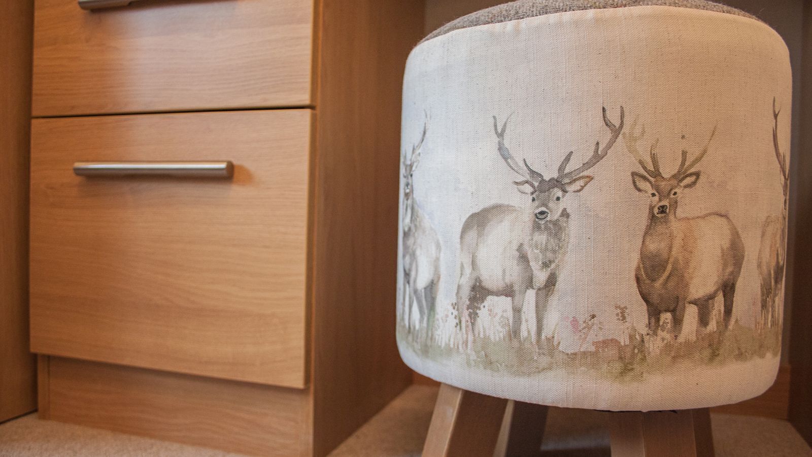 Un mueble de madera con dos cajones y una butaca de tela con un diseño de ciervo.