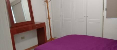 Ein Schlafzimmer mit einem Bett, einem hölzernen Schminktisch, einem Spiegel und einem Kleiderständer.