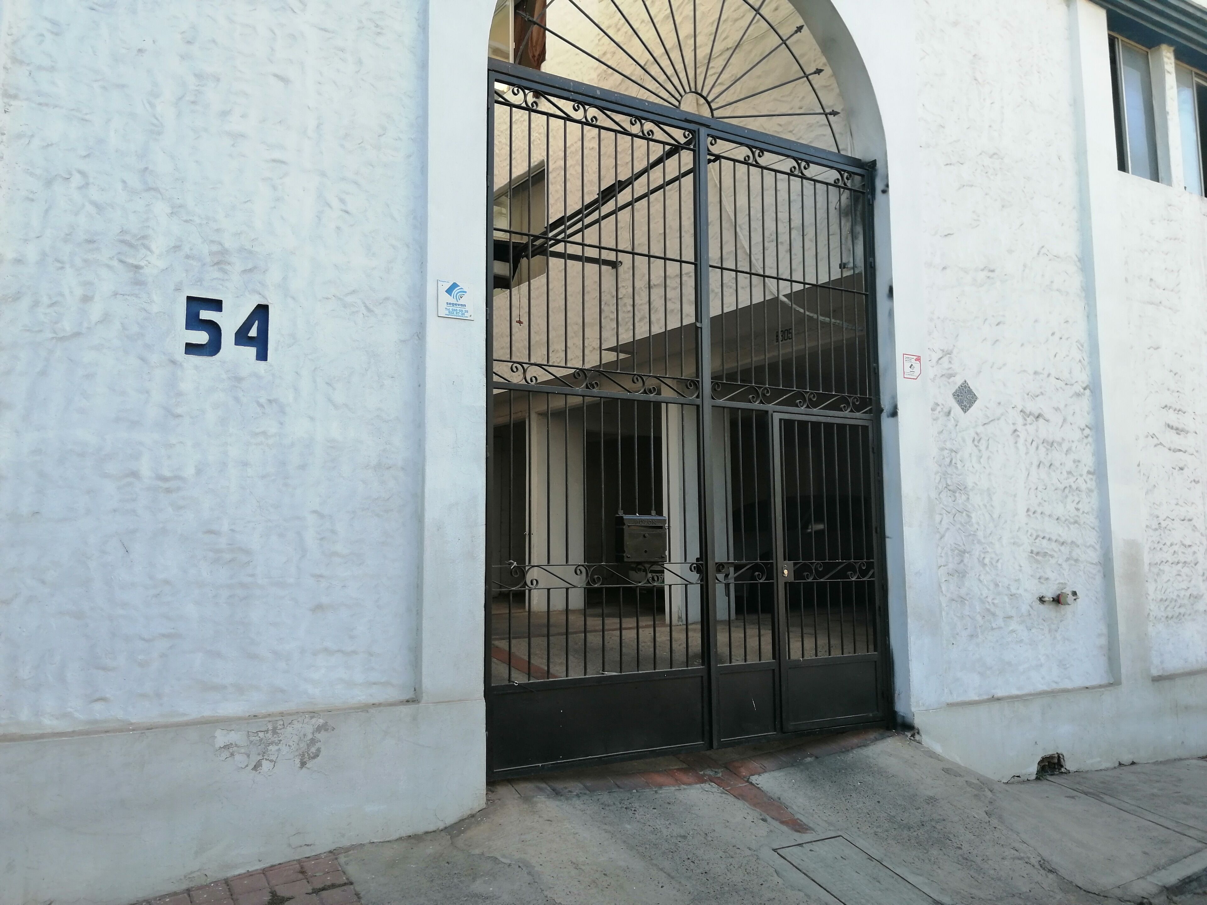 A gated entrance with a number '54' on the wall, a metal gate, and a building with a white exterior.
