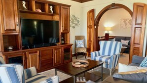 Una sala de estar con un televisor de pantalla plana grande, armarios de madera, sillones a rayas, una mesa de centro y una decoración con una estrella de mar.