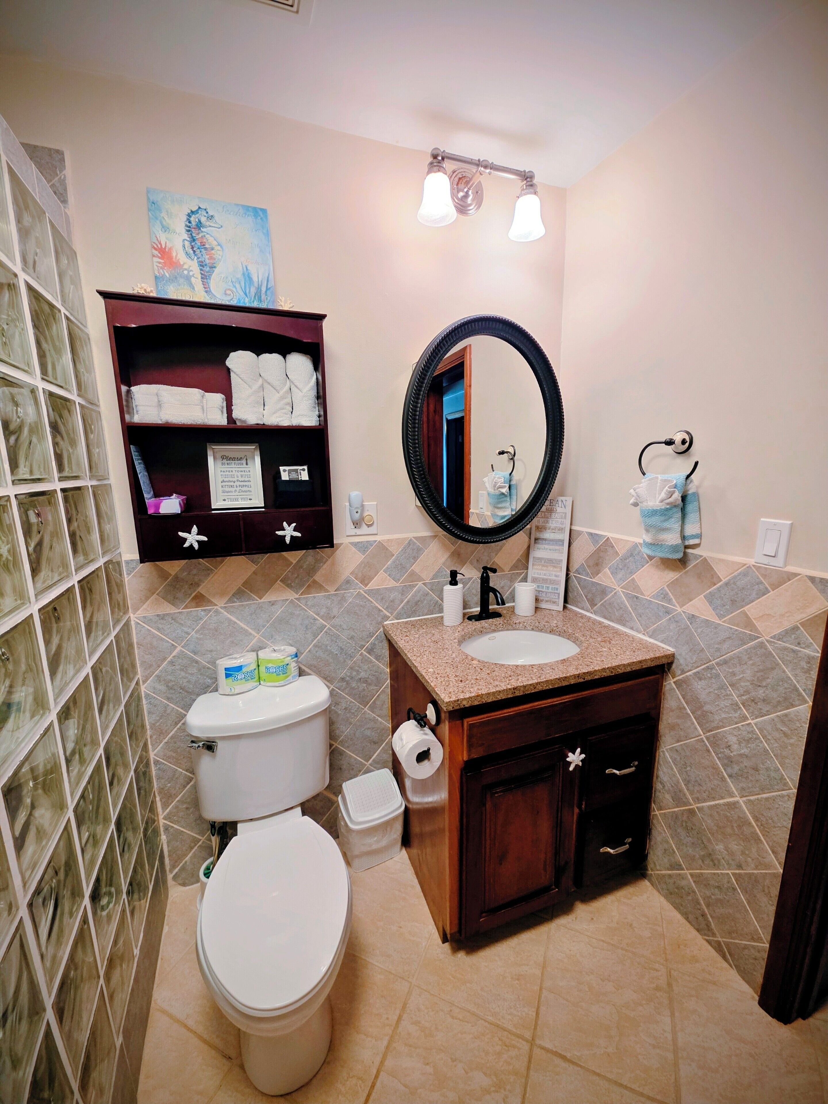 A bathroom with a toilet, sink, and mirror. There is a towel rack and a shelf with towels.