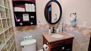 A bathroom with a toilet, sink, and mirror. There is a towel rack and a shelf with towels.