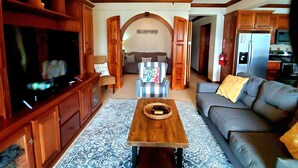 Una sala de estar con un mueble de madera para entretenimiento, un sofá, una mesa de centro y una cocina al fondo.
