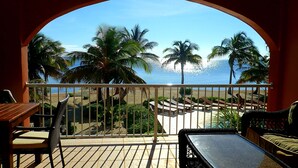 Un balcón con vistas a la playa, palmeras y un cielo despejado.