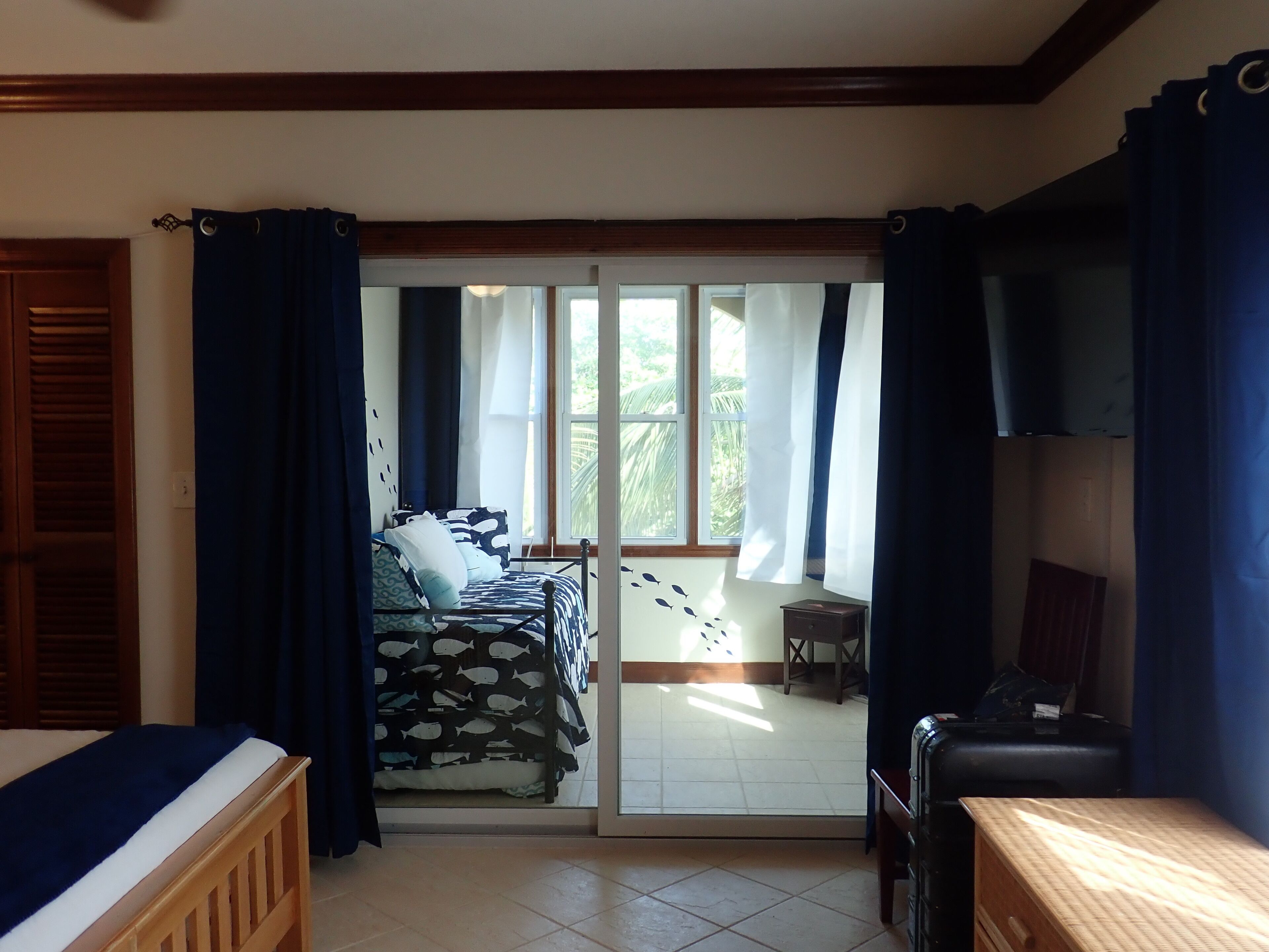 A room with a bed, a desk, and a view through a sliding door to an outdoor area with a table and chairs.