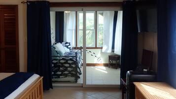 A room with a bed, a desk, and a view through a sliding door to an outdoor area with a table and chairs.