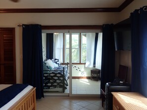 A room with a bed, a desk, and a view through a sliding door to an outdoor area with a table and chairs.