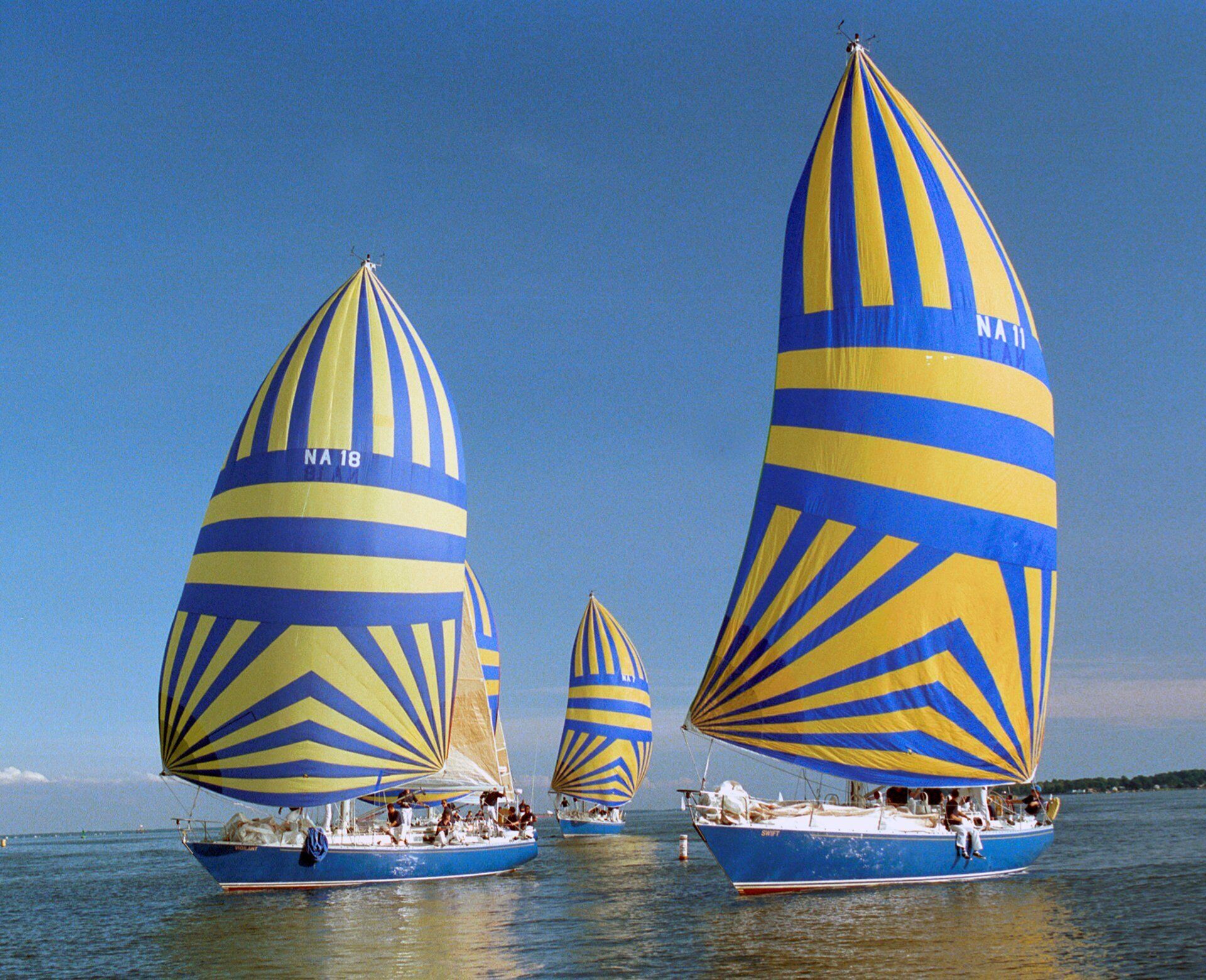 Three sailboats with blue and yellow striped sails on calm water.