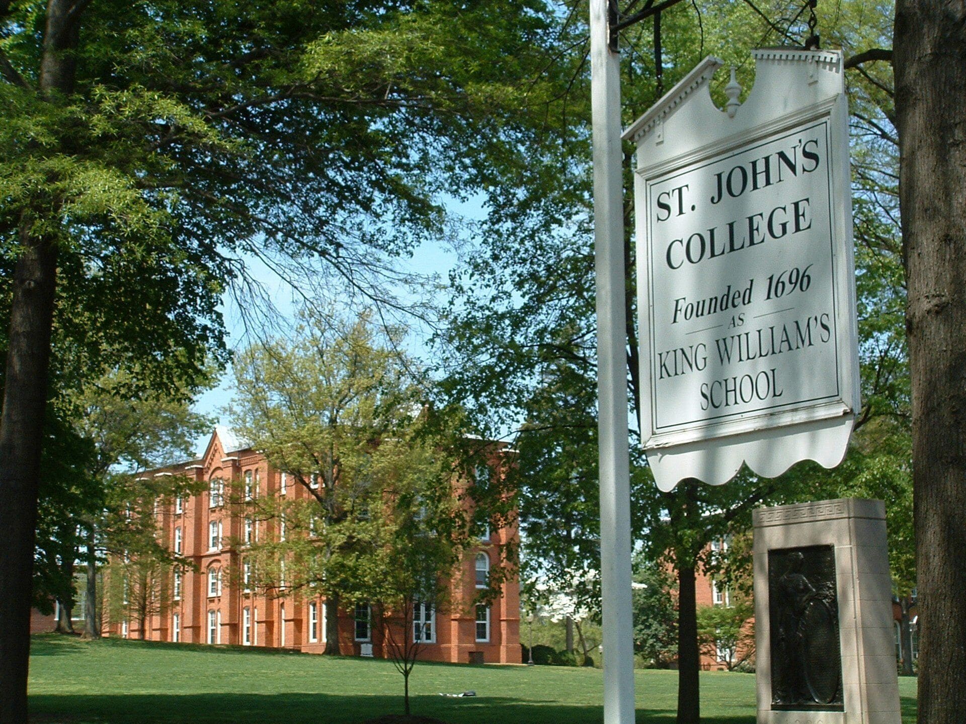 Señal de St. John's College con un fondo histórico, un edificio de ladrillo rojo y una estatua en primer plano.
