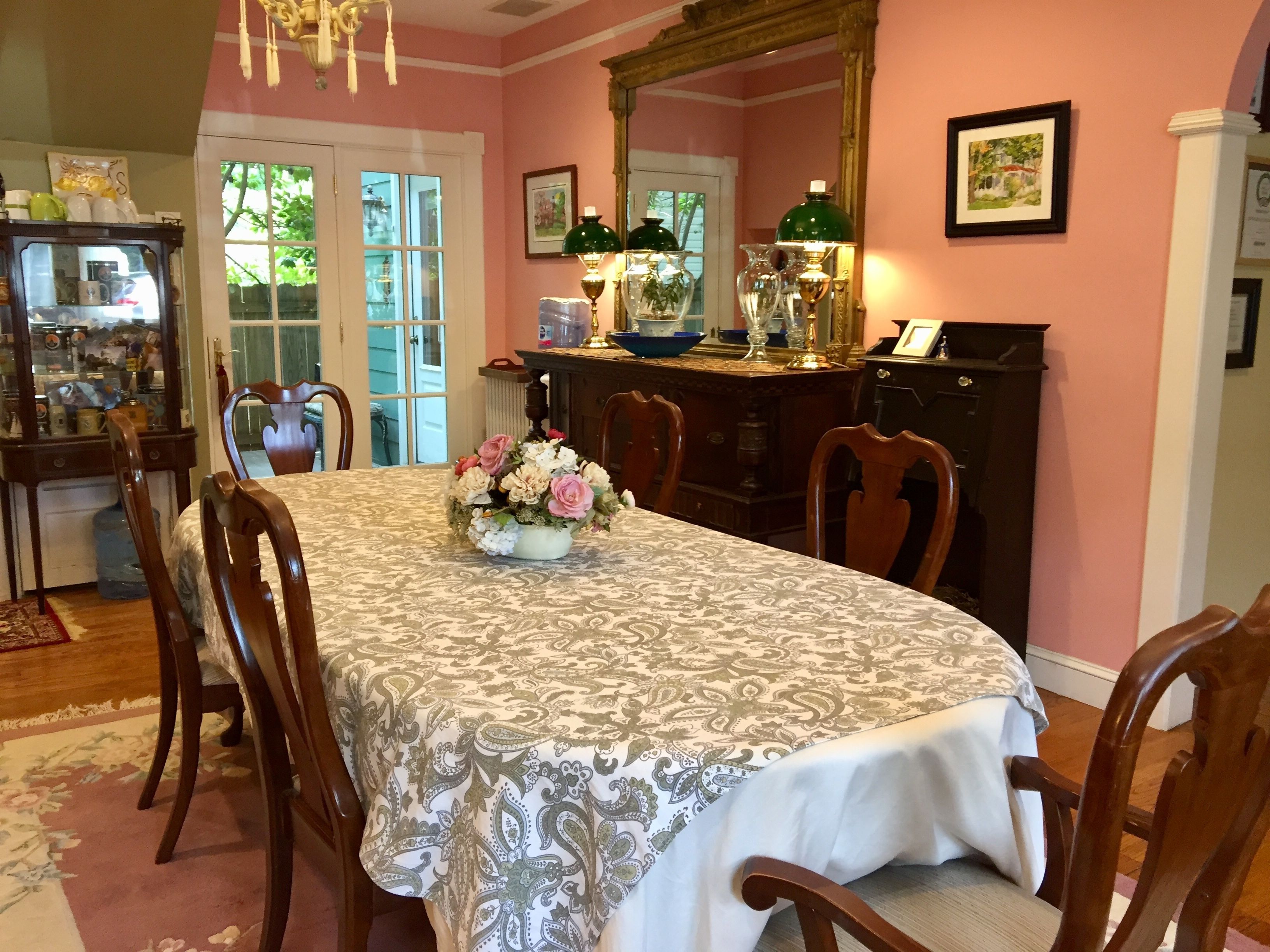 A dining room with a table set for four, surrounded by wooden chairs. A vase of flowers is placed on the table.