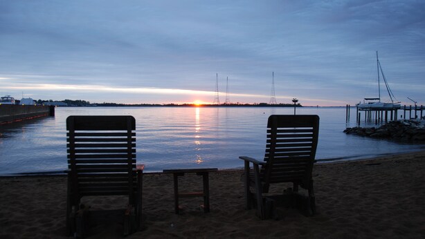 Two wooden chairs facing a calm body of water at sunset. - Inn at Horn Point (Annapolis)