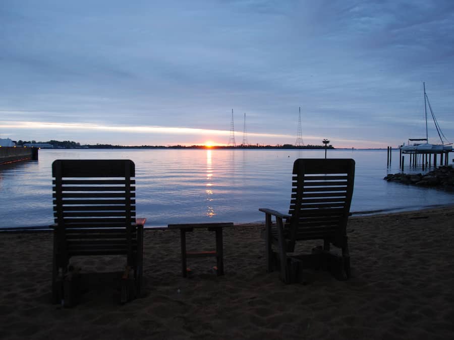 Two wooden chairs facing a calm body of water at sunset.