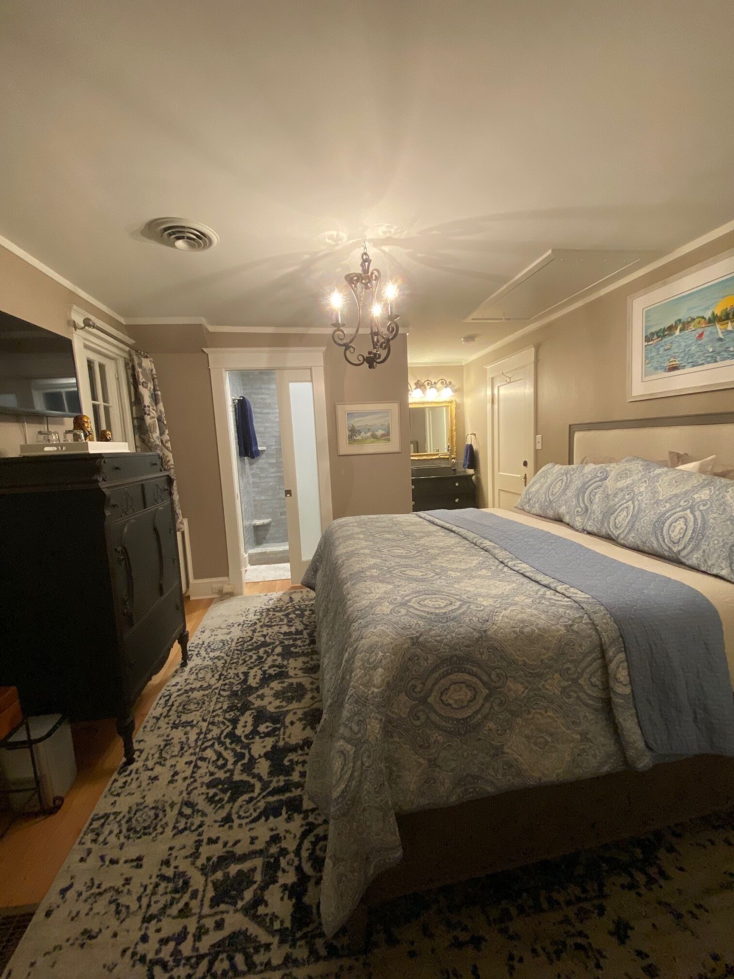 A bedroom with a bed, dresser, and a chandelier.