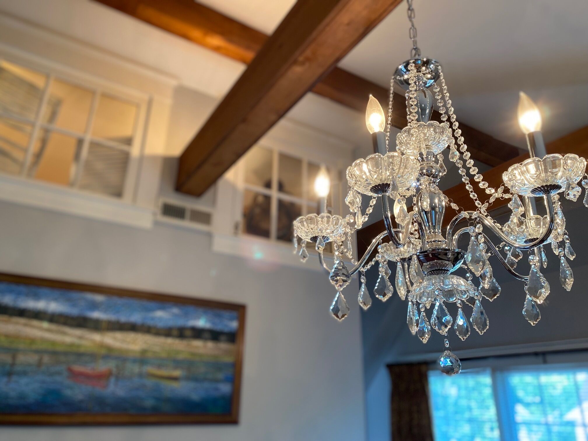 A chandelier with multiple arms and crystal decorations in a room with wooden beams and a painting on the wall.
