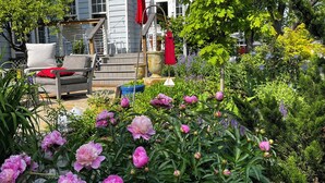 A house with a porch, a red umbrella, and a garden with pink flowers. - Inn at Horn Point (Annapolis)