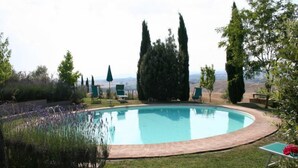 Une piscine dotée d’une terrasse en bois, entourée de verdure et de grands arbres.