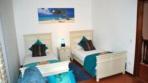 Een slaapkamer met twee bedden, een nachtkastje met een lamp en een schilderij van een strand.