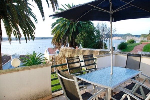 A patio with a table and chairs, overlooking a body of water and hills.