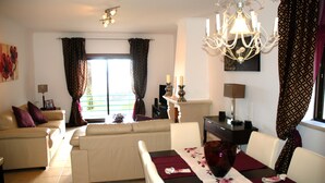 Een woonkamer met een bank, eettafel, kroonluchter en gordijnen.