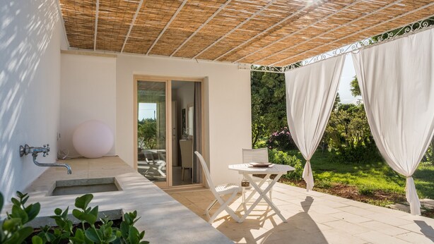 A covered outdoor area with a table and chairs, a water feature, and a view of greenery. - Tenuta DonnAnna (Galatone)