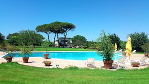 A swimming pool with lounge chairs and potted plants, surrounded by a well-maintained lawn and trees. - Tenuta DonnAnna (Galatone)