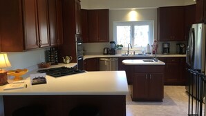 Una cocina moderna con armarios de madera oscura, una isla central con dos taburetes, horno empotrado y refrigerador de acero inoxidable.
