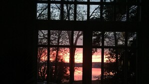 Una ventana con vista a un atardecer sobre el agua, enmarcada por una cuadrícula de vidrios.