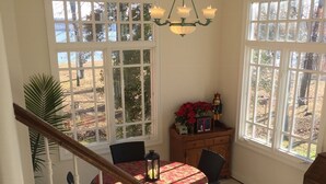 Un comedor con una mesa dispuesta para cuatro, una araña y grandes ventanales que ofrecen vistas al exterior.