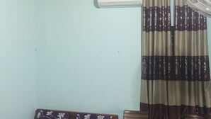 Una habitación pequeña con cama, ventilador y ventana con cortinas.