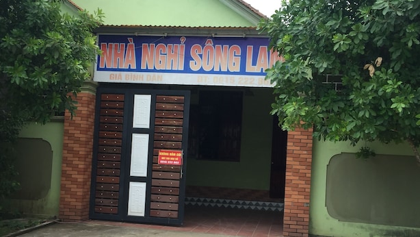 Entrada de un edificio con un cartel, una pared de ladrillo y una puerta verde.
