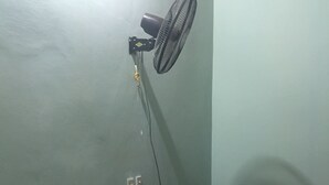 Una habitación pequeña con una mesa y cuatro sillas, un ventilador de pared y un enchufe.