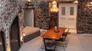 Une façade en pierre, une table et des chaises en bois, une porte et un escalier menant à l’étage supérieur.