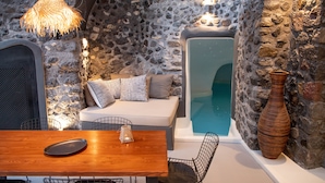 Une pièce aux murs de pierre, avec une table en bois, un luminaire en fibres tressées, un banc blanc rembourré et un grand vase.