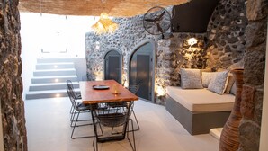 Une pièce aux murs de pierre, avec une table et des chaises en bois, un canapé et un ventilateur.