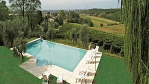 Ein rechteckiger Pool mit glasklarer, blauer Wasseroberfläche, umgeben von einer Rasenfläche mit mehreren Liegestühlen und einem kleinen Tisch.