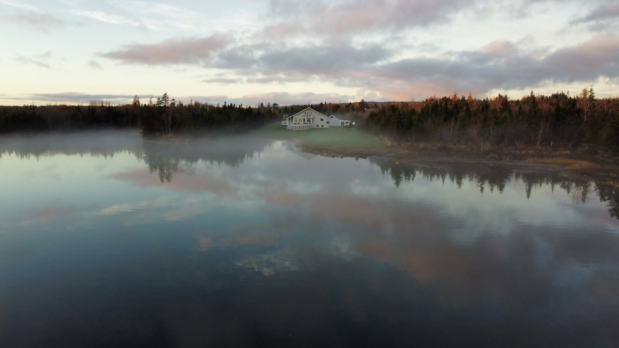 Una casa a la vora d'un llac tranquil amb un bosc al fons.