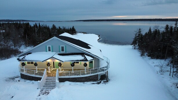 Una casa cubierta de nieve con un muelle de madera y un embarcadero que da a una barca, rodeada por un bosque y un lago.