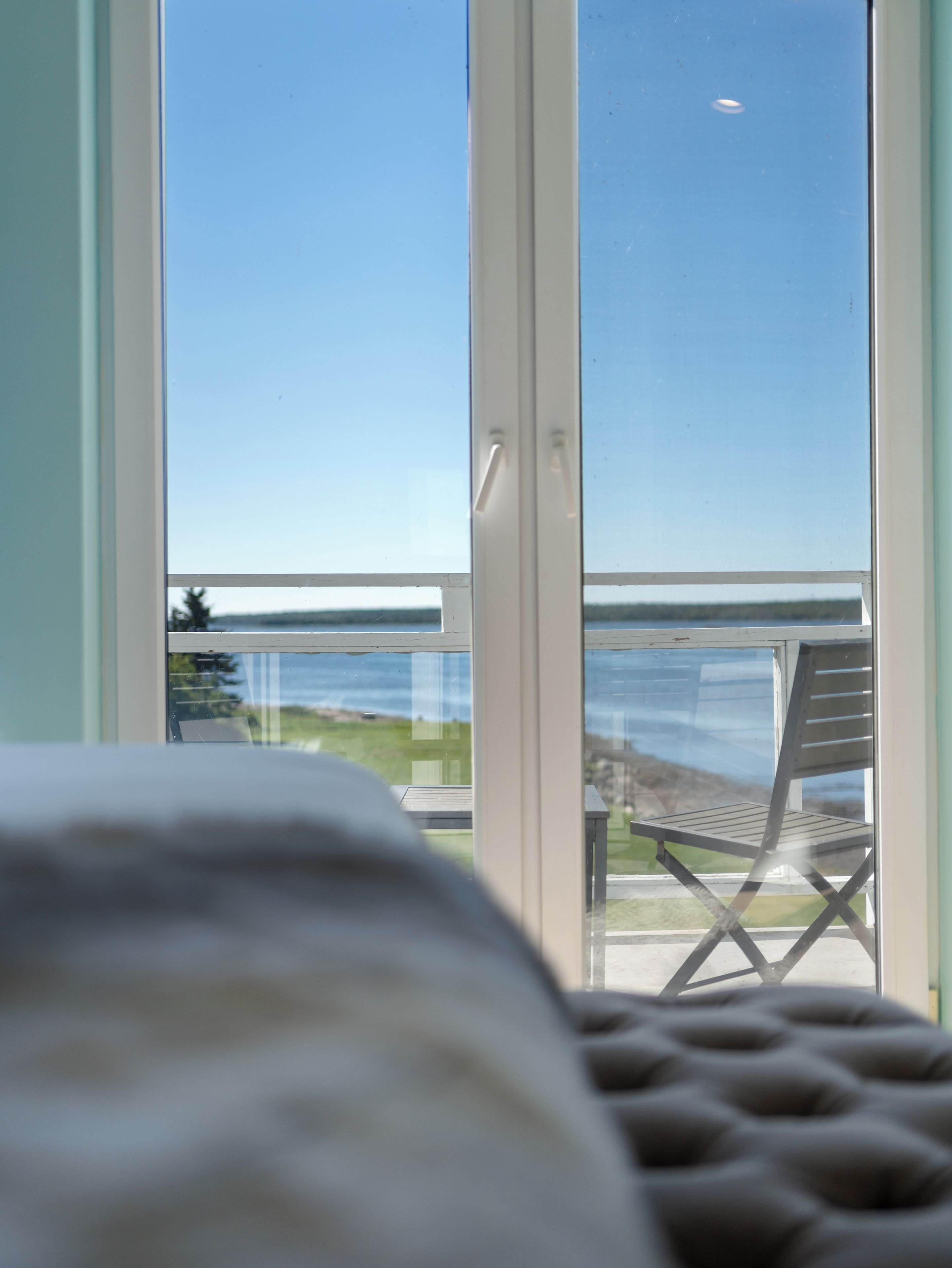 Vista desde una habitación con ventana que da a un balcón con una silla y una mesa.