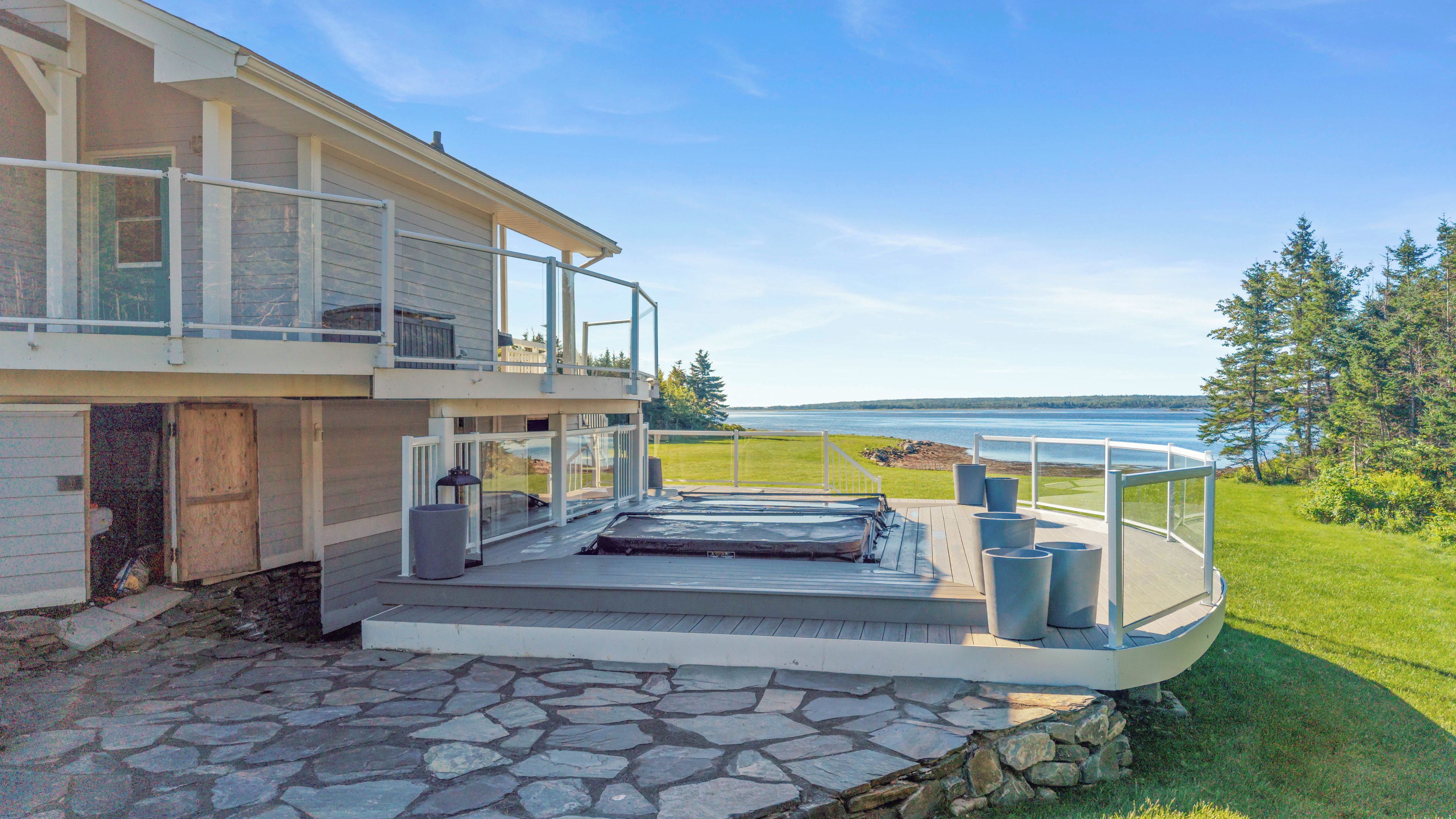 Una casa moderna con un patio de piedra, un balcón con barandilla y vistas a un lago.