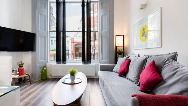 A modern living room with a grey sofa, a wooden coffee table, and a TV mounted on the wall.