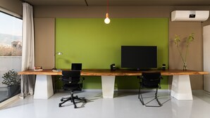 Un espacio de oficina moderno con un escritorio de madera, dos sillas de oficina negras, un monitor de pantalla plana grande, un aire acondicionado blanco y un colgador de techo.