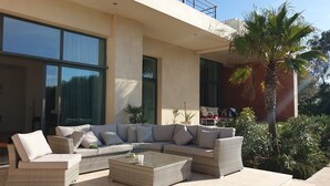 Un espacio exterior moderno con un sofá modular, dos mesas auxiliares y una palmera.